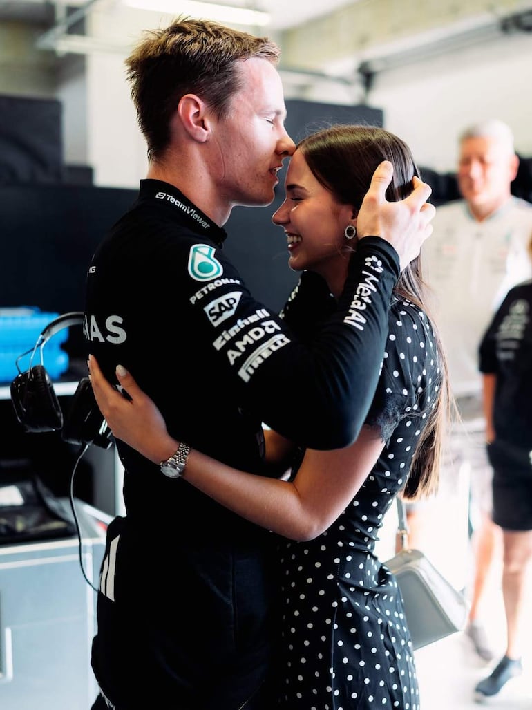 Joshua Duerksen en mono negro abraza a Anneke Rahn, vestida con vestido negro con puntos blancos, ambos sonriendo en un garaje.