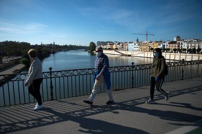 La gente cruza el Puente de Triana en Sevilla el 2 de mayo de 2020, durante las horas permitidas por el gobierno para salir y hacer ejercicio, por primera vez desde el comienzo de un bloqueo nacional para prevenir la propagación de la enfermedad COVID-19.