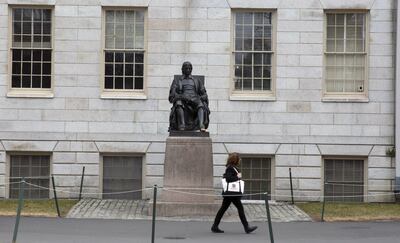 Una mujer camina junto a la estatua de John Harvard en el patio de Harvard en Cambridge, Massachusetts.