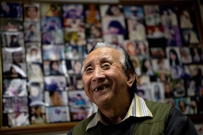 Esta foto tomada el 17 de diciembre de 2019 muestra al casamentero Zhu Fang sonriendo en su casa con paredes cubiertas de imágenes de mujeres solteras que han acudido a él a lo largo de los años en Beijing.