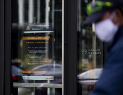 Una persona con tapabocas camina junto a un letrero pidiéndole a las personas que no ingresen si se sienten enfermos o si han estado en contacto con un paciente con coronavirus (COVID-19), en el campus del centro de Amazon, en Seattle, Washington.