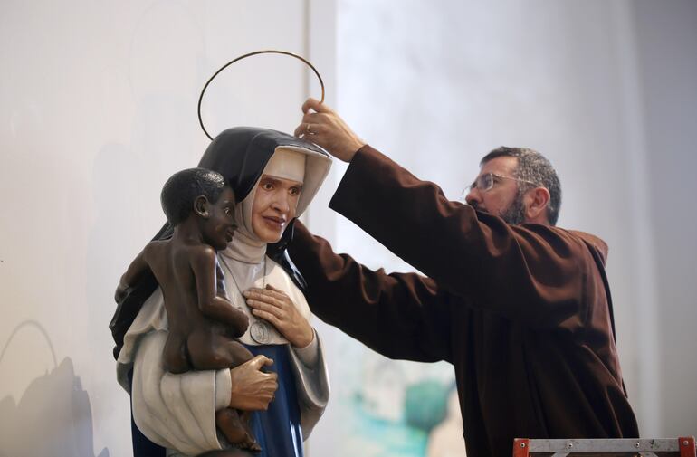 Un sacerdote coloca una aureola sobre una escultura con la imagen de la Irma Dulce (Hermana Dulce), considerada la "Madre Teresa de Calcuta brasileña" y la primera mujer nacida en Brasil declarada santa, durante una vigilia por su canonización este domingo, en Salvador (Brasil). 