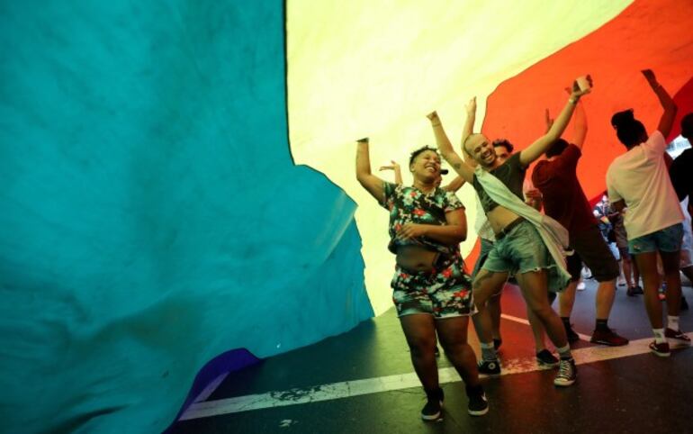 Un grupo de personas baila bajo la bandera de la comunidad LGBTIQ en la playa de Copacabana, en Río de Janeiro.