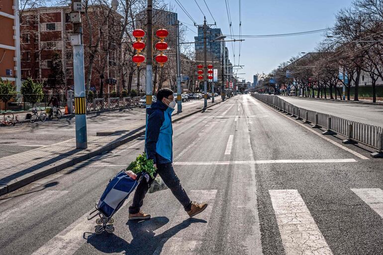 Un hombre con tapabocas lleva sus compras por una calle de Pekín, China.