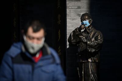 Una estatua de bronce porta con una máscara en la entrada de una tienda a lo largo de una calle comercial en Beijing hoy, 4 de febrero.