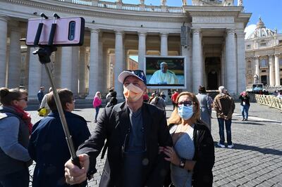 Una pareja se toma fotografías en la plaza de San Pedro mientras el Papa hace su oración dominical del Angelus, esta vez por medio de la pantalla.