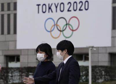 Peatones con tapabocas caminan cerca de un emblema de los JJ.OO., en Tokio. El evento sigue programado iniciar el 24 de julio.