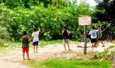 Niños juegan a volar la pandorga en una calle de arena en la zona del Banco San Miguel. Se empujan, corretean, se abrazan.
