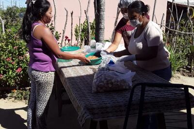 Una madre de familia consigue retirar comida en un recipiente de plástico parecido a una palangana.