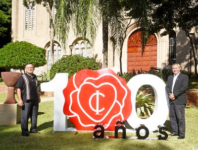 El pastor Roberto Martínez y el director Víctor Hugo Penayo, junto con el logo que marca los 100 años del Colegio Internacional.