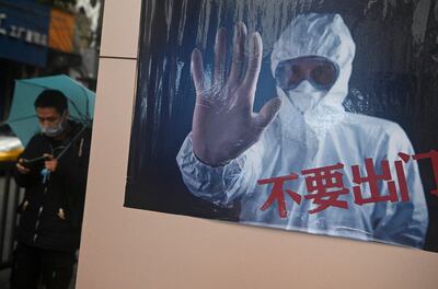 Un hombre con una máscara pasa al costa de un poster que reza "No salgas", en Jiujiang, China.