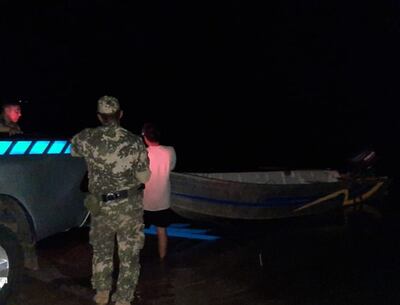 Un efectivo de la Prefectura Naval de Ayolas vigila a uno de los pescadores arrestados mientras saca su bote del agua.