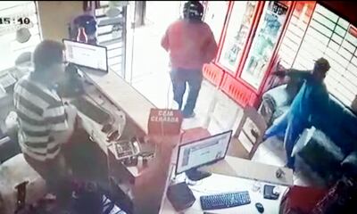 Uno de los asaltantes apunta con un revólver al cajero del negocio asaltado en Juan Manuel Frutos, Caaguazú.