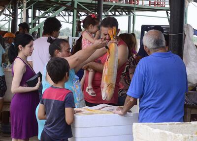 Una vendedora de pescado  exhibe un dorado a un cliente. Cientos de personas aprovecharon el ultimo día para comprar especies frescas. pues desde hoy rige la veda pesquera.