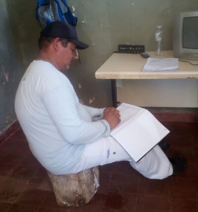 El funcionario de la planta de tratamiento de la Essap en Yataity toma apuntes de su trabajo sentado sobre un tronco.