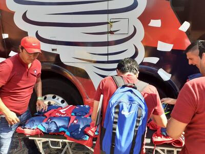 Los encargados de las vestimentas subiendo los equipos al bus que será utilizado como vestuario.