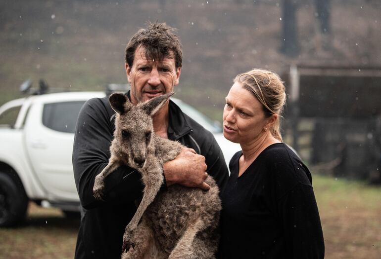 Gary Henderson (a la izquierda) alza a un pequeño canguro lastimado que él y su compañera Sara Tilling están cuidando hasta que se recupere.