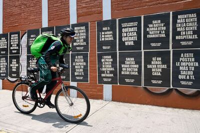 Un ciclista que trabaja como delivery pasa con su bicicleta cerca de unos afiches con información sobre el coronavirus en México.