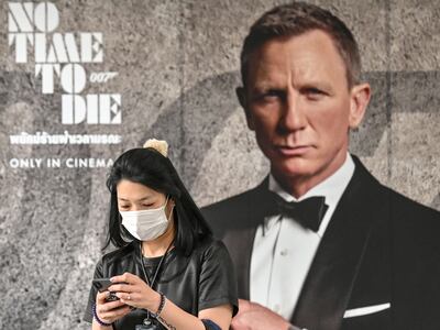 El estreno de la nueva película del agente James Bond, "Sin tiempo para morir", fue pospuesto a noviembre. En la fotografía se observa a una mujer en Bangkok, con un tapabocas, frente a uno de los carteles del filme.