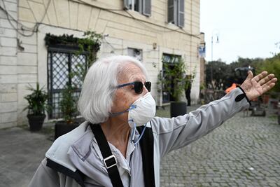 En esta foto de archivo tomada el 17 de marzo de 2020, una mujer de 83 años con una máscara facial hace gestos mientras sale a comprar comida en el centro de Roma.