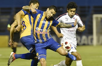 Los luqueños Aldo Quiñónez y Joel Benítez frenan la marcha del delantero albo David Fleitas, anoche en la victoria de Sportivo Luqueño sobre Nacional 2-0 en Villa Elisa.