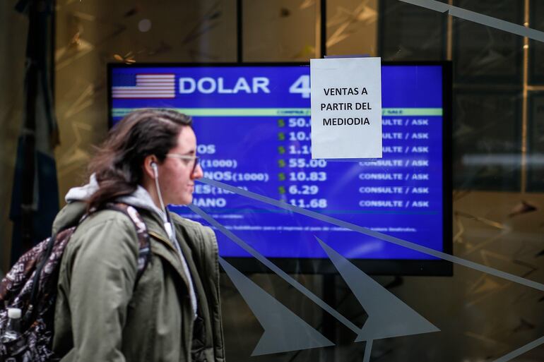 Una mujer camina frente a un tablero que muestra los valores de cambio del dólar este lunes, en Buenos Aires (Argentina).