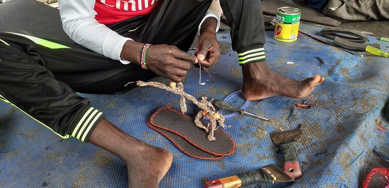 Un hombre termina de confeccionar los adornos que van cosidos a un zapato de neumático en el mercado Konyo Konyo en Yuba. Les dicen "mutu kelei", lo que en el dialecto árabe de Yuba significa "morirás y ellas seguirán", zapatillas hechas a partir de neumáticos viejos que se han convertido en una solución económica y tan dura como la vida en Sudán del Sur, pero con un encanto y estilo particulares.