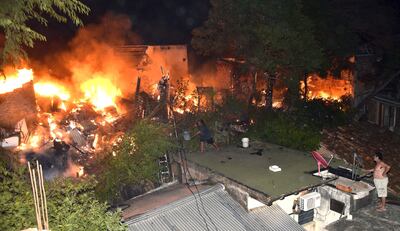 Un solitario hombre intenta desesperadamente combatir las feroces llamas arrojando agua desde un balde, sobre el techo de una vivienda.
