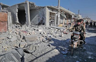 Dos personas en motocicleta pasan frente a los escombros de un edificio dañado por bombardeos en la aldea siria de Maasaran.