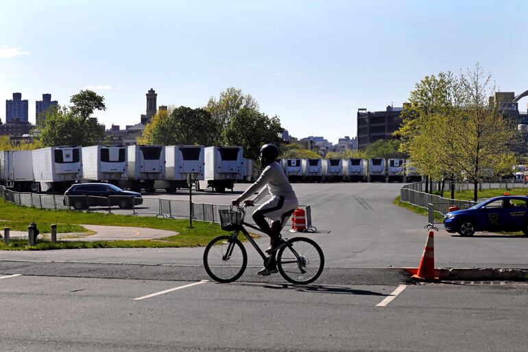 Una persona se desplaza en bicicleta frente a camiones de refrigeración que serán enviados a hospitales como depósito de cadáveres, en Randall's Island, en Nueva York (EE.UU).