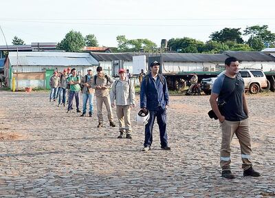 Los funcionarios forman fila antes de ingresar a la fábrica, a fin de que sean sometidos a  un chequeo para detección de fiebre.