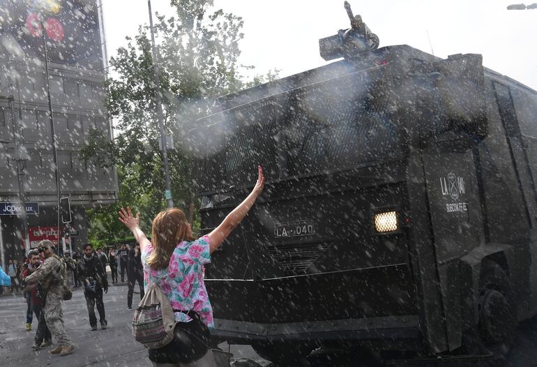 Una mujer intenta detener a un vehículo militar durante un enfrentamiento entre manifestantes y policías en Santiago, el sábado.