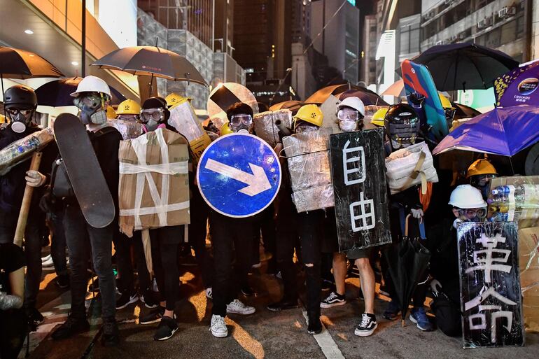 Un grupo de manifestantes se cubre con escudos caseros, incluidos skates y señales de tránsito. 