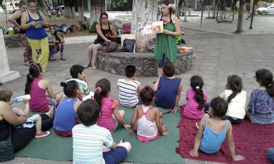 Una mujer muestra un libro de cuentos a un grupo de niños en una plaza de Villa Elisa.