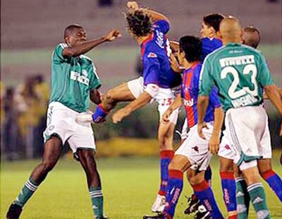 La pierna derecha levantada de “Aquiles” Báez que impactará en el bajo vientre del brasileño Douglas cuyo manotazo no llegó a destino. Batalla campal en São Paulo.