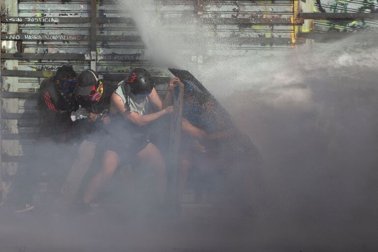Manifestantes en Santiago de Chile se protegen de un chorro de agua disparado por los Carabineros para dispersarlos.