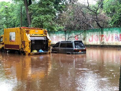 Una camioneta y un camión recolector de basura, varados en una calle inundada de Ciudad del Este.