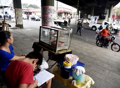 Una vendedora ambulante observa el trabajo de los policías que verifican a los ocupantes de vehículos, mientras su hijo completa su lección.