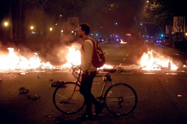 Un hombre camina junto a una barricada de fuego en la Gran Vía durante los disturbios tras la concentración este miércoles de miles de personas ante la consellería de Interior en Barcelona en el tercer día de movilizaciones de protesta contra las condenas a los líderes del procés. 