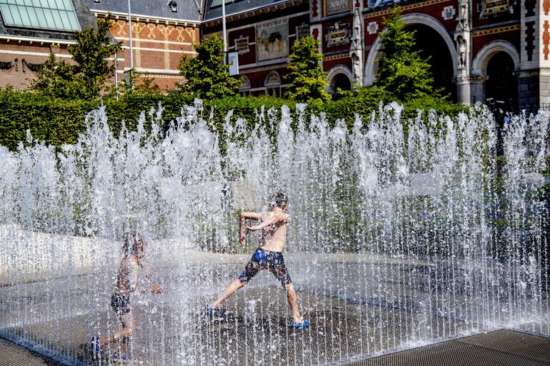 La gente juega y se refresca en la fuente de la plaza Museumplein, en Amsterdam, Holanda, para combatir la ola de calor. 