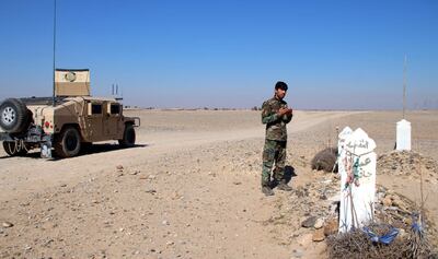 Un soldado afgano reza junto a una tumba mientras los oficiales de seguridad patrullan en Helmand, Afganistán.