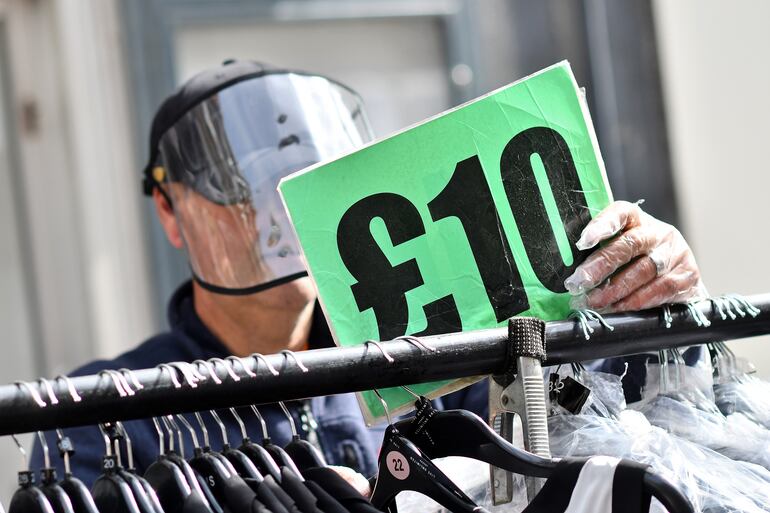 Un vendedor con una máscara de protección coloca un cartel en su puesto de venta en el mercado de Petticoat Lane, en Londres.