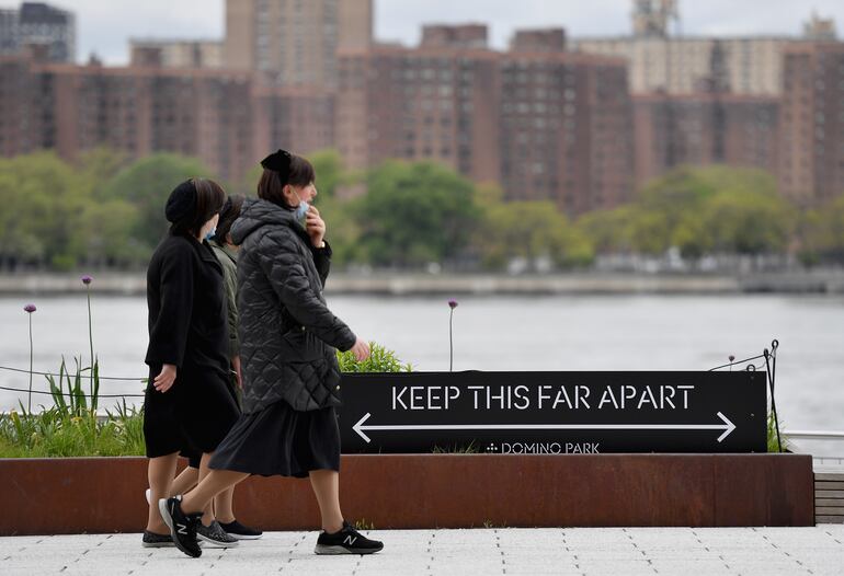 Mujeres caminan junto a un cartel que indica la distancia adecuada entre personas durante el aislamiento social, en Brooklyn, Nueva York.