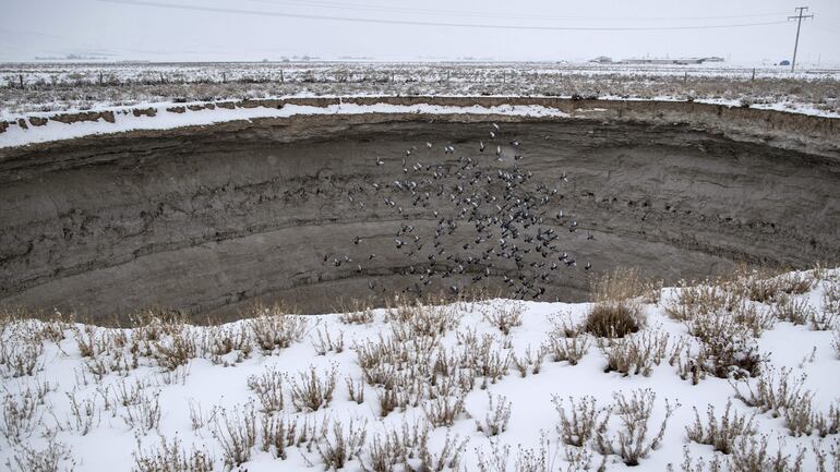 Una bandada de aves vuela sobre un agujero negro en la tierra sobre un campo nevado cerca de Sandikli en la villa de Karapinar.