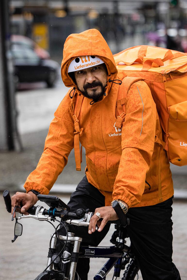 Equipado para protegerse de la lluvia, el exministro afgano y hoy repartidor en Alemania, Sayed Sadaat, pedalea su bicicleta. 