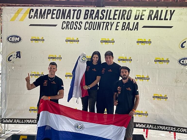 Óscar Santos y Mirna Pereira (centro), posan en lo más alto del podio tras vencer en la categoría T3 FIA con el UTV Can Am Maverick X3 y culminar terceros en la clasificación general entre los autos en el Rally de Barretos, disputado el fin de semana en Brasil.
