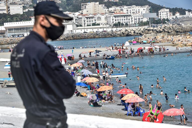 Un policía con mascarilla observa a una multitud en una playa en Argel, Argelia.