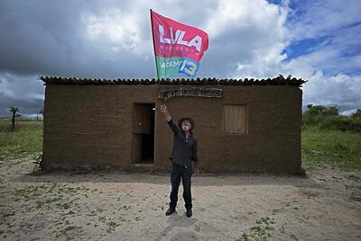 Eraldo dos Santos, primo del candidato presidencial de Brasil por el izquierdista Partido de los Trabajadores (PT) y expresidente (2003-2010) Luiz Inácio Lula Da Silva, ondea una bandera afuera de una réplica de la choza derrumbada hace mucho tiempo donde Lula nació hace 76 años afuera del ciudad de Caetes, en el estado de Pernambuco.