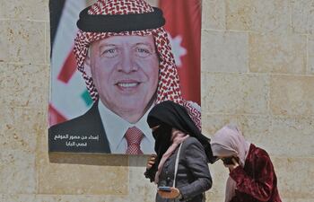 Dos mujeres caminan junto a un cartel con el retrato del rey Abdalá II de Jordania, en Amán.