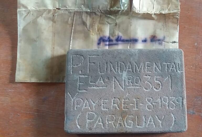 La placa de piedra con la inscripción, y la hoja que lo acompañaba en el interior del cofre enterrado bajo el piso de la escuela.
